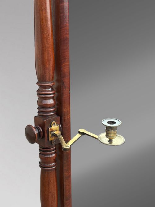 fig 4. An early 19th-century Regency mahogany cheval mirror featuring turned uprights, brass candle sconces, finials, and splayed legs on brass castors.