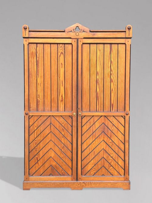 fig 1. A late 19th-century pitch pine Arts and Crafts wardrobe featuring vertical slatted upper door panels, chevron lower panels, and a carved cresting rail.
