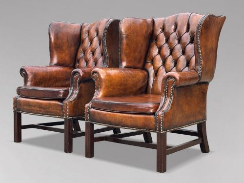 fig 1. A pair of late Victorian wingback armchairs upholstered in deep-buttoned tan brown leather with brass stud trimming and dark wooden legs.