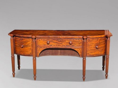 fig 1. An antique 19th-century William IV mahogany sideboard featuring reeded fluted legs, line inlay, and a central drawer above an arched recess.