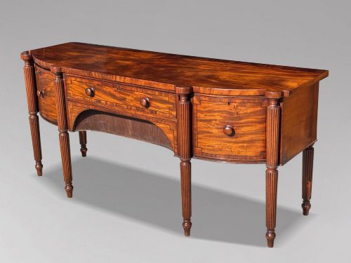 fig 2. An antique 19th-century William IV mahogany sideboard featuring reeded fluted legs, line inlay, and a central drawer above an arched recess.