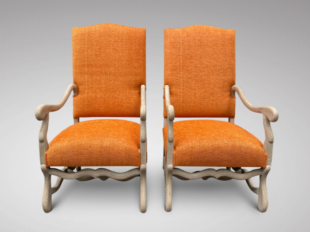 A pair of 19th-century French walnut armchairs featuring carved light wood frames, open arms, serpentine stretchers, and bright orange textured fabric upholstery.
