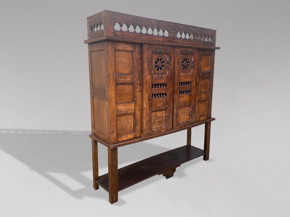 A 19th-century carved dark wood Breton cupboard featuring spindle turnings, openwork geometric wheel motifs, and a gallery top raised on tall straight legs with an under-shelf.