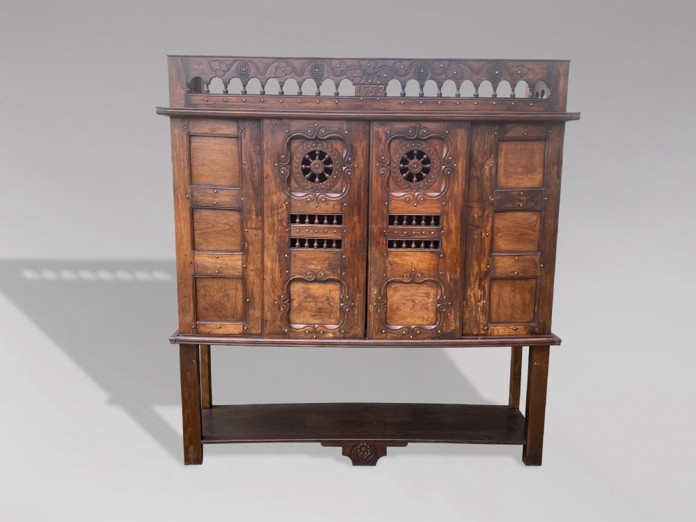 A 19th-century carved dark wood Breton cupboard featuring spindle turnings, openwork geometric wheel motifs, and a gallery top raised on tall straight legs with an under-shelf. View II