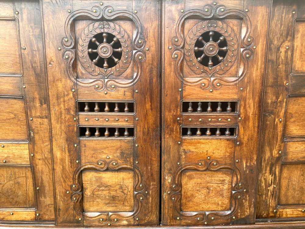 A 19th-century carved dark wood Breton cupboard featuring spindle turnings, openwork geometric wheel motifs, and a gallery top raised on tall straight legs with an under-shelf. View V