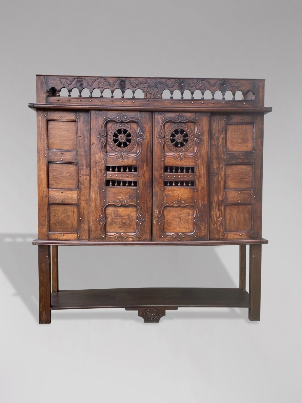 A 19th-century carved dark wood Breton cupboard featuring spindle turnings, openwork geometric wheel motifs, and a gallery top raised on tall straight legs with an under-shelf. View VI