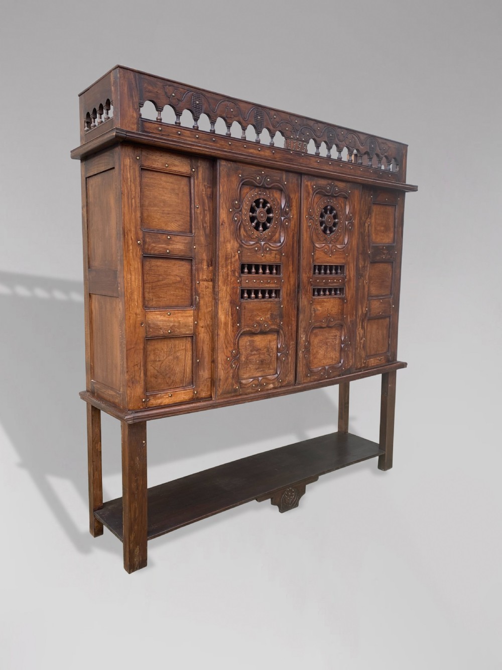 A 19th-century carved dark wood Breton cupboard featuring spindle turnings, openwork geometric wheel motifs, and a gallery top raised on tall straight legs with an under-shelf. View VII