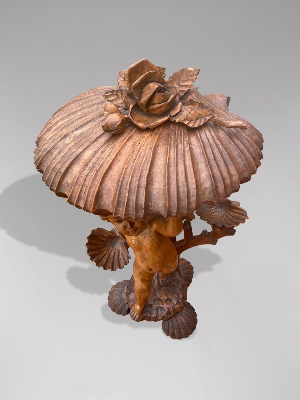 A 19th-century carved wooden figure of a winged putto holding a large scallop shell basin overhead while standing on a shell-shaped base. View II