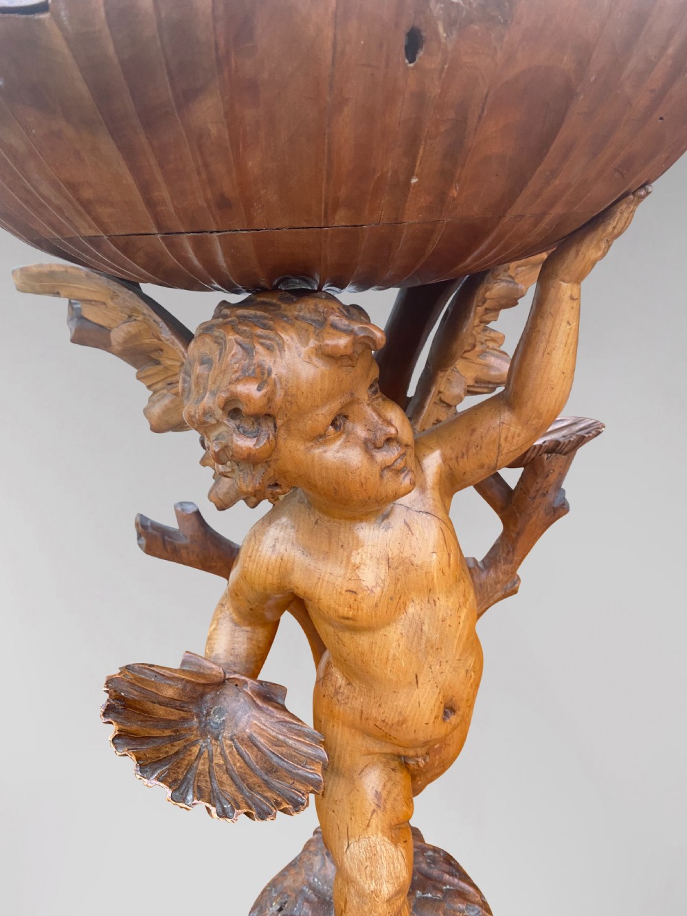 A 19th-century carved wooden figure of a winged putto holding a large scallop shell basin overhead while standing on a shell-shaped base. View VII