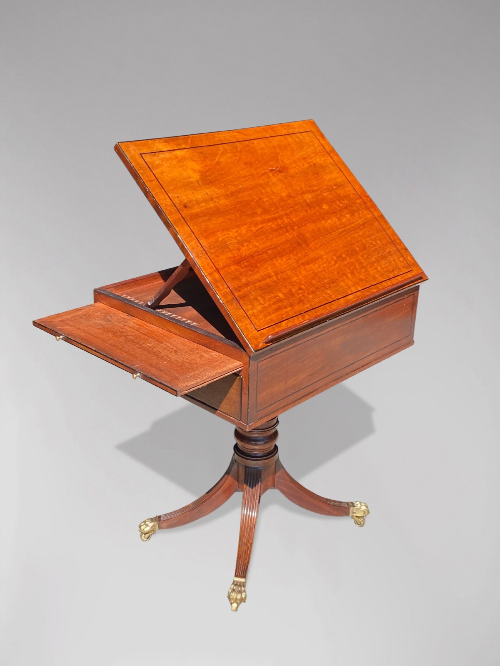 A George III mahogany reading table featuring an adjustable tilted top, a side drawer, a turned pedestal stem, and reeded tripod legs with brass paw feet. View IV