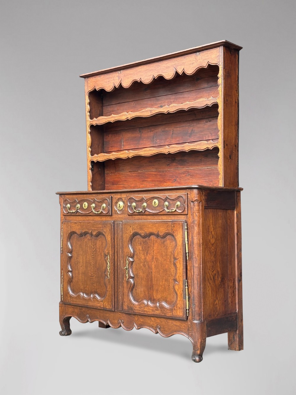 An 18th-century French provincial walnut buffet vaisselier featuring a two-door cabinet with carved panels and drawers beneath an open three-shelf plate rack with scalloped friezes.