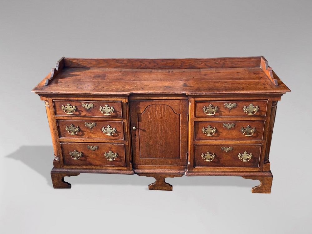 An 18th-century Lancashire oak dresser base featuring brass handles, a central cupboard door, six drawers, and shaped bracket feet. View II