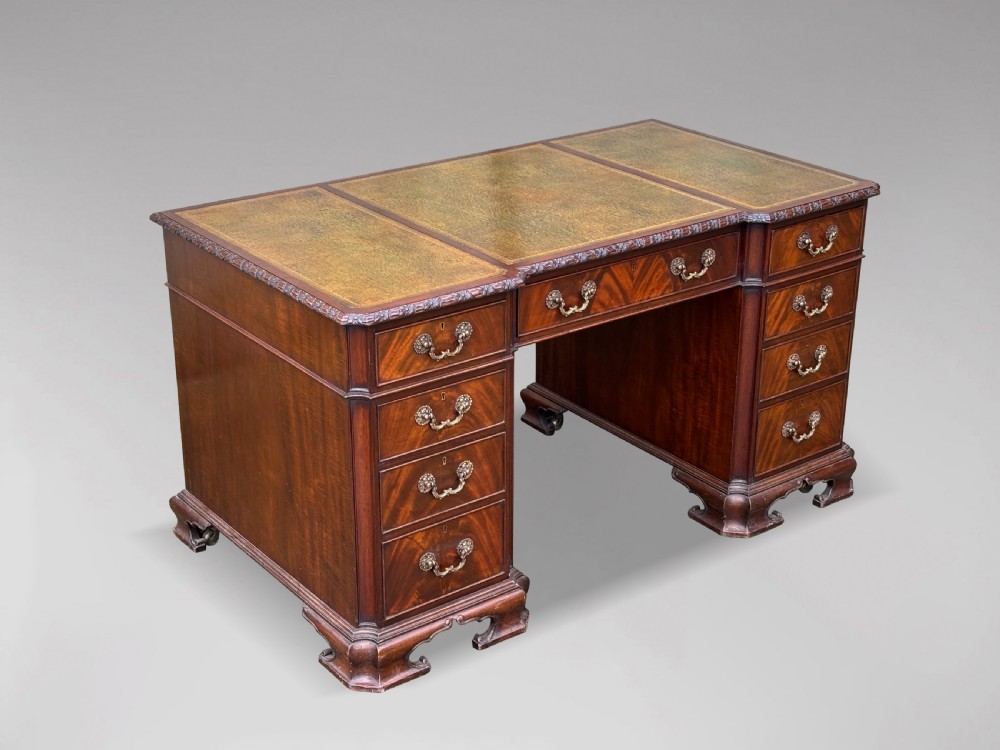 A nineteenth-century Chippendale style mahogany pedestal desk featuring a three-panel green leather writing top, nine drawers with brass handles, and bracket feet.