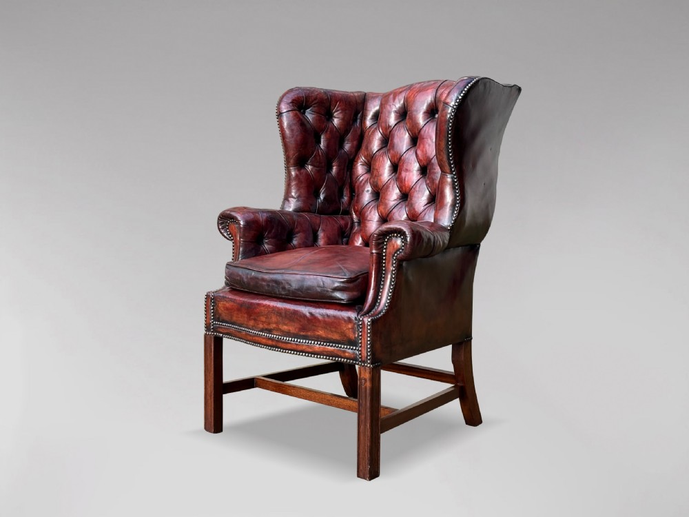 A 19th-century button-backed wingback armchair upholstered in deep burgundy leather with brass stud detailing and wooden legs.