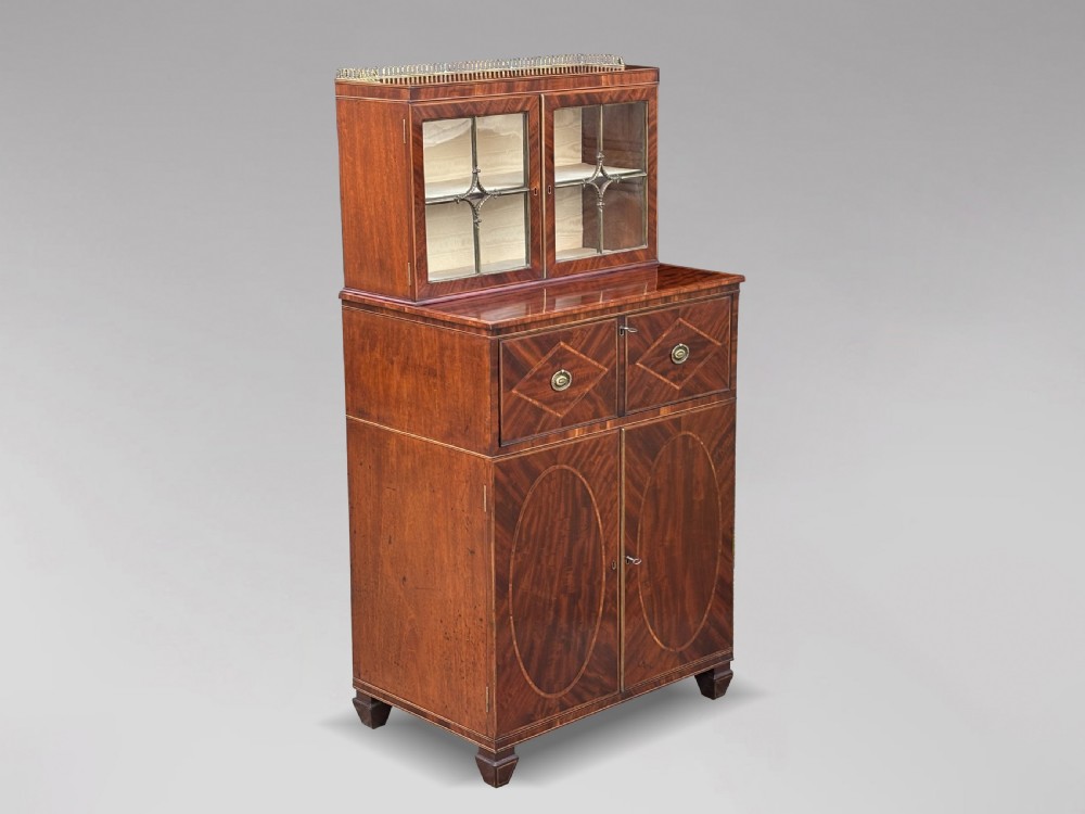 A 19th-century Regency mahogany secretaire bookcase featuring a top brass gallery, geometric glazed doors, two drawers, and oval flame-mahogany veneer panel doors below.