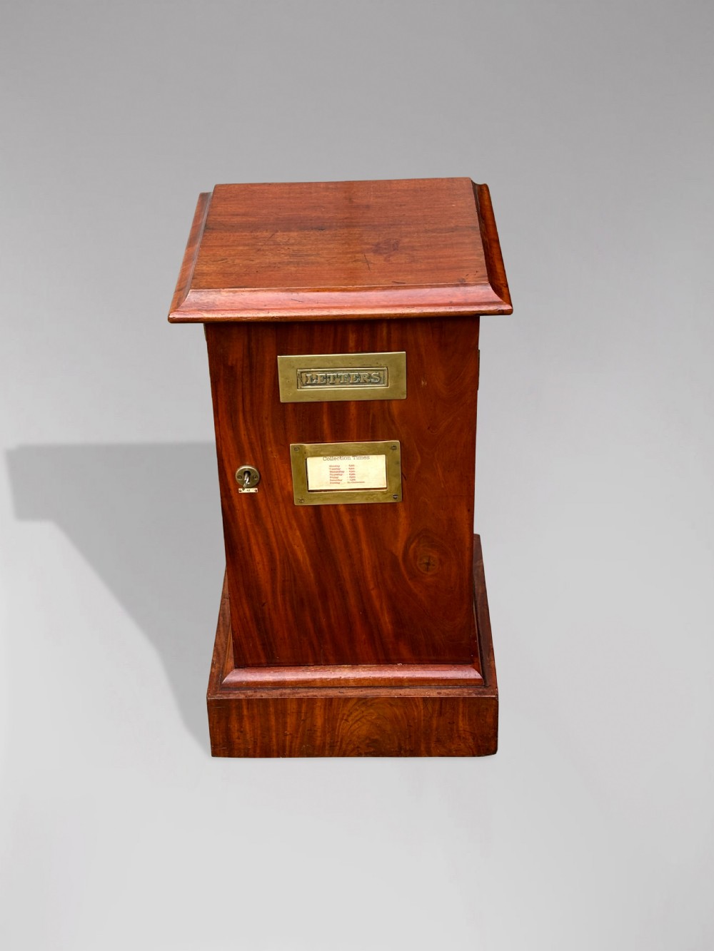 A 19th-century mahogany post box with a molded lid, brass letter slot, collection times plaque frame, and front key lock. View III