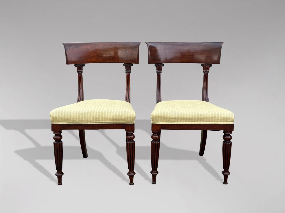 A pair of 19th-century William IV mahogany side chairs featuring curved top rails, fluted turned front legs, and pale yellow upholstered seats.