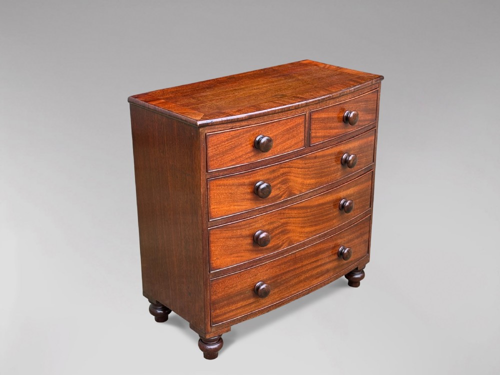 A nineteenth-century miniature mahogany bowfront chest of drawers featuring turned wooden knobs and bun feet.