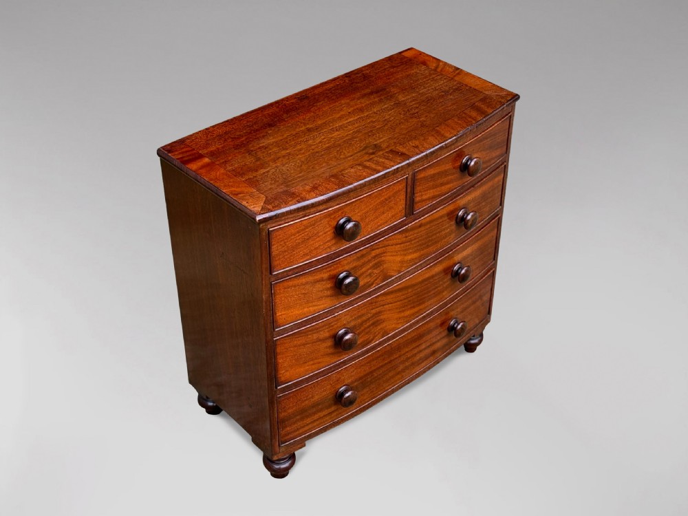 A nineteenth-century miniature mahogany bowfront chest of drawers featuring turned wooden knobs and bun feet. View II