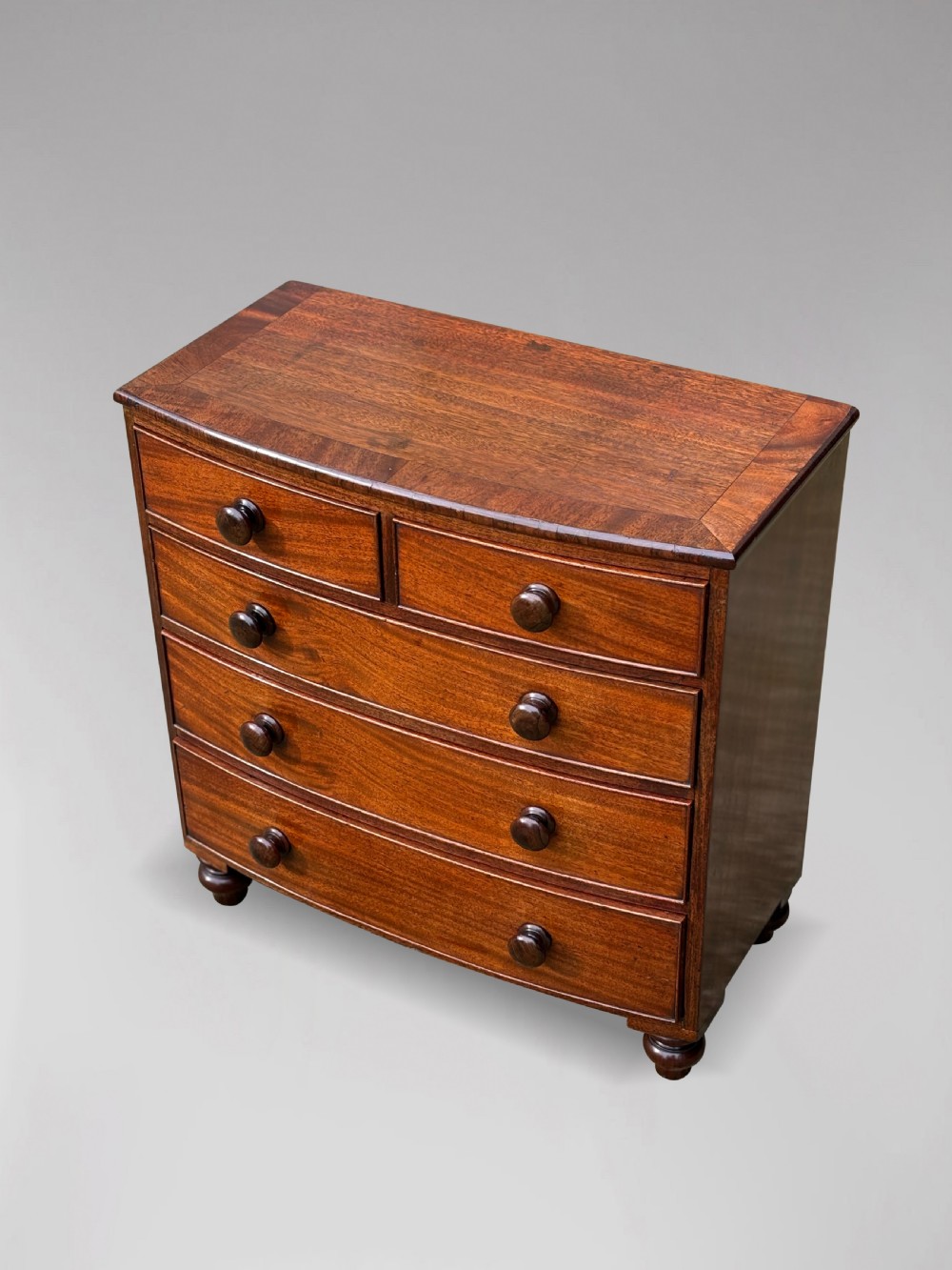 A nineteenth-century miniature mahogany bowfront chest of drawers featuring turned wooden knobs and bun feet. View III