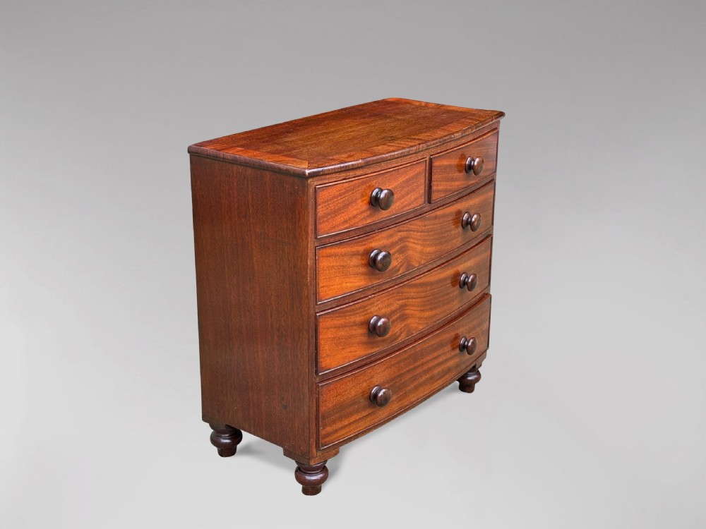 A nineteenth-century miniature mahogany bowfront chest of drawers featuring turned wooden knobs and bun feet. View V