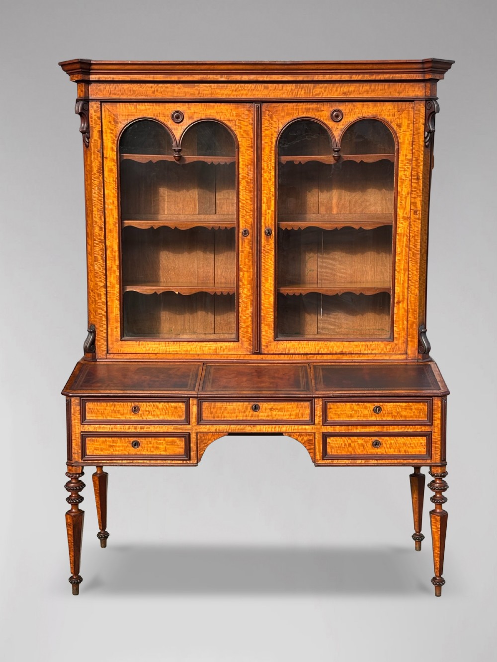 A 19th-century French maple bureau bookcase featuring a top glazed two-door display section above a kneehole writing desk with leather inset panels and turned legs. View X