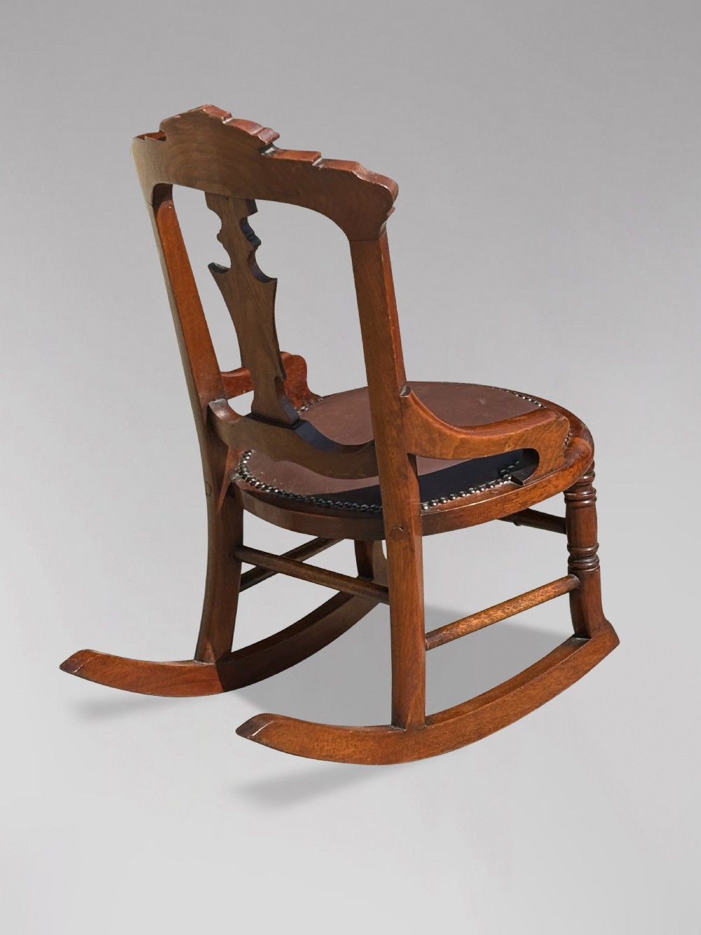 A 19th-century Victorian childs wooden rocking chair featuring a carved backrest with burr wood inlay, a brown leather padded seat with brass stud details, and turned front legs on curved rockers. View III