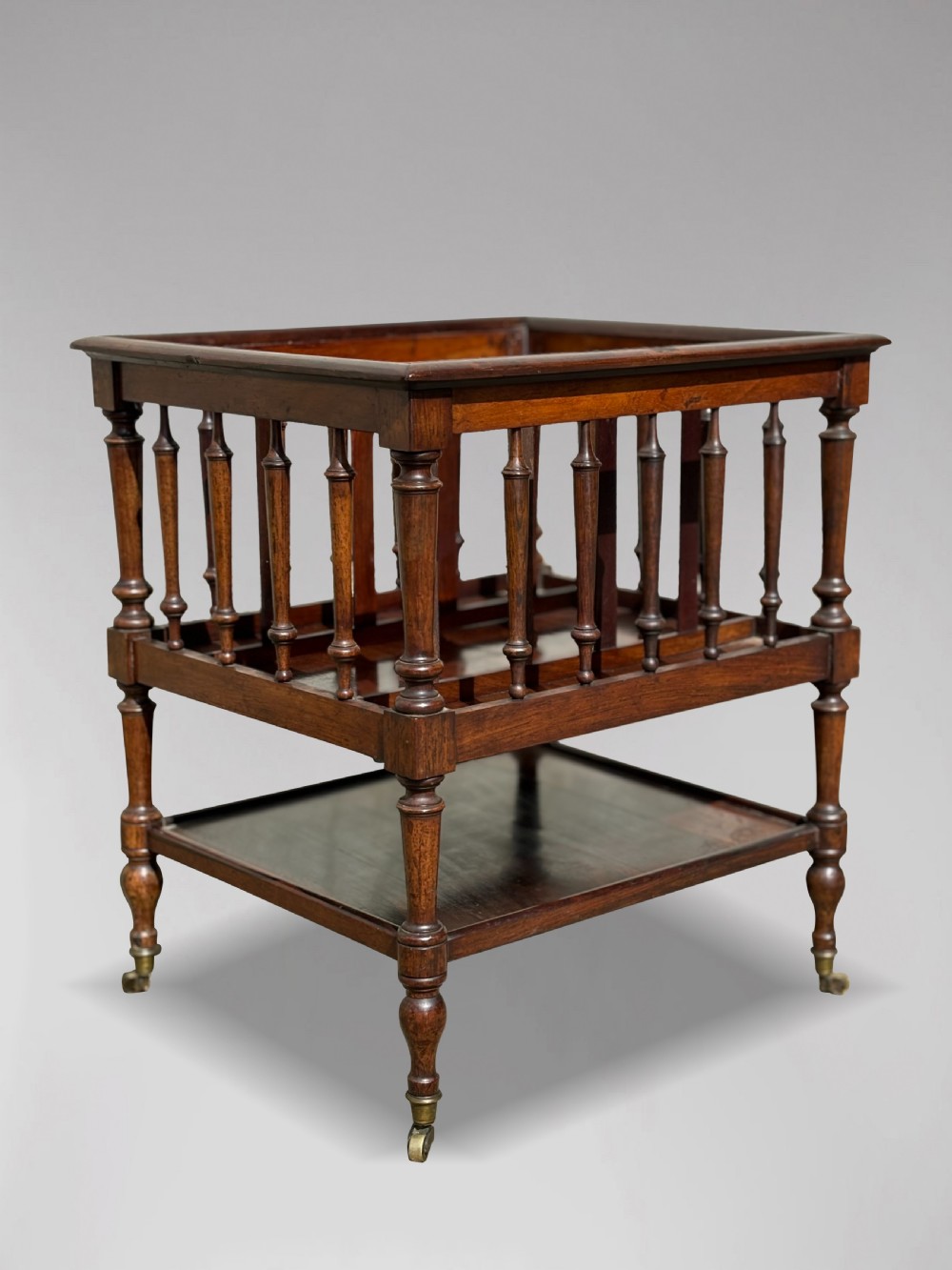 A nineteenth-century dark rosewood canterbury featuring turned spindle supports, divided upper compartments, a lower open shelf, and brass castors. View II