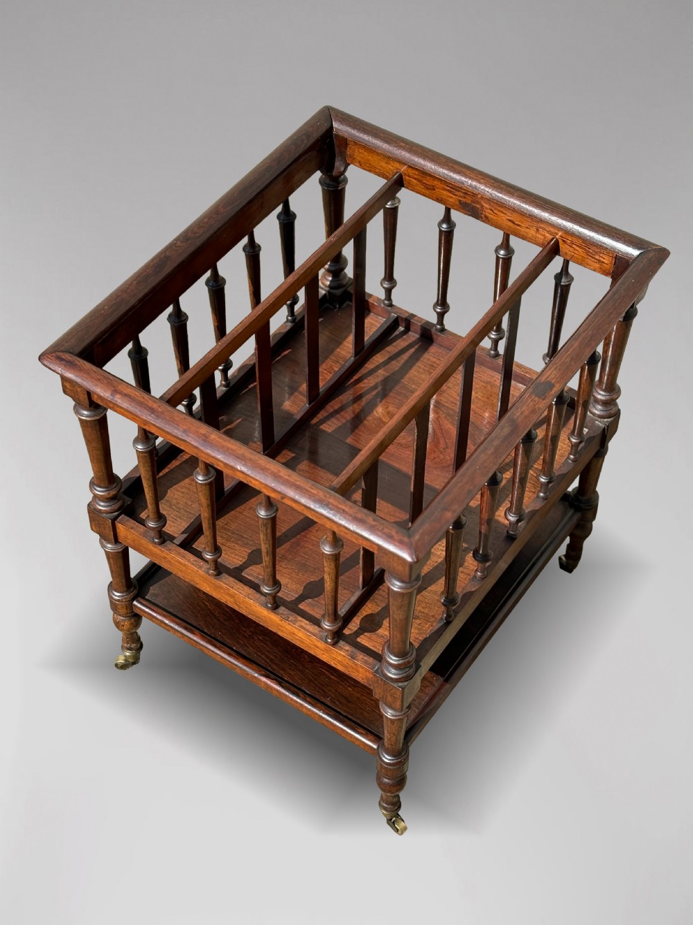 A nineteenth-century dark rosewood canterbury featuring turned spindle supports, divided upper compartments, a lower open shelf, and brass castors. View IV