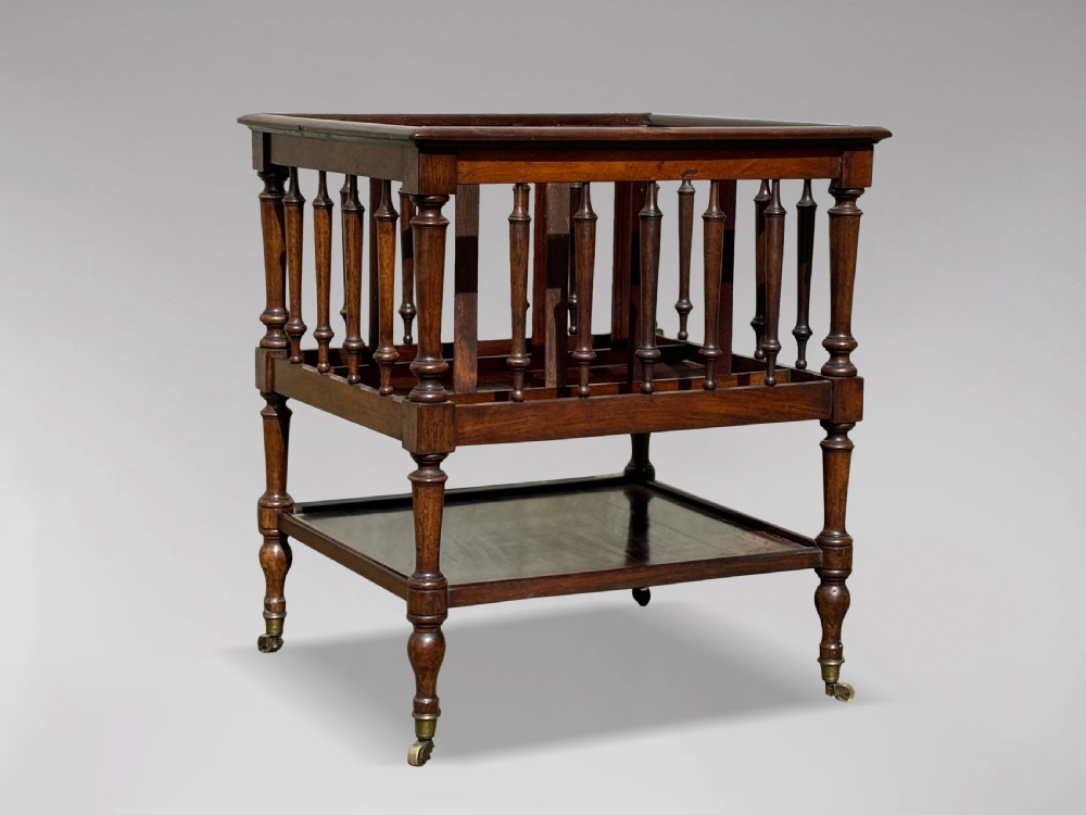 A nineteenth-century dark rosewood canterbury featuring turned spindle supports, divided upper compartments, a lower open shelf, and brass castors. View V