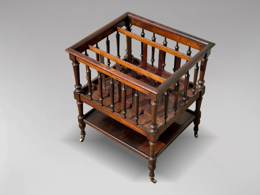 A nineteenth-century dark rosewood canterbury featuring turned spindle supports, divided upper compartments, a lower open shelf, and brass castors. View VI