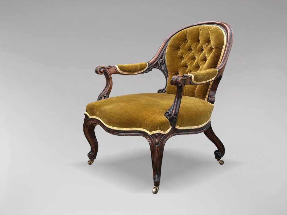 A 19th-century Victorian mahogany armchair upholstered in tufted olive green velvet with carved scroll arms and cabriole legs on brass castors.