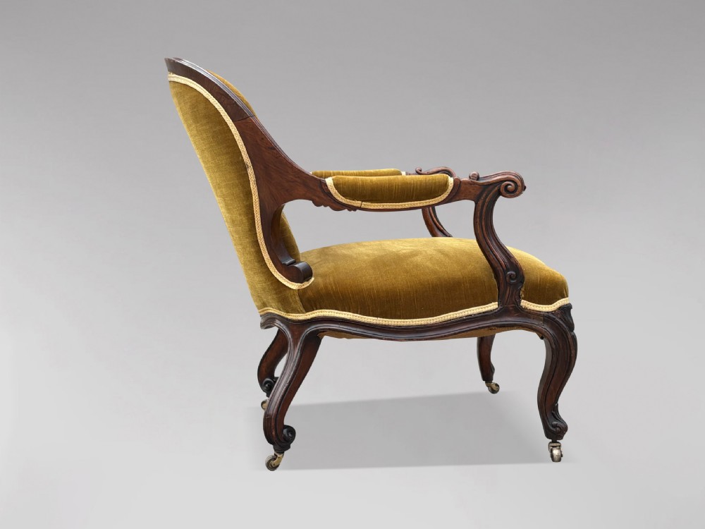 A 19th-century Victorian mahogany armchair upholstered in tufted olive green velvet with carved scroll arms and cabriole legs on brass castors. View II