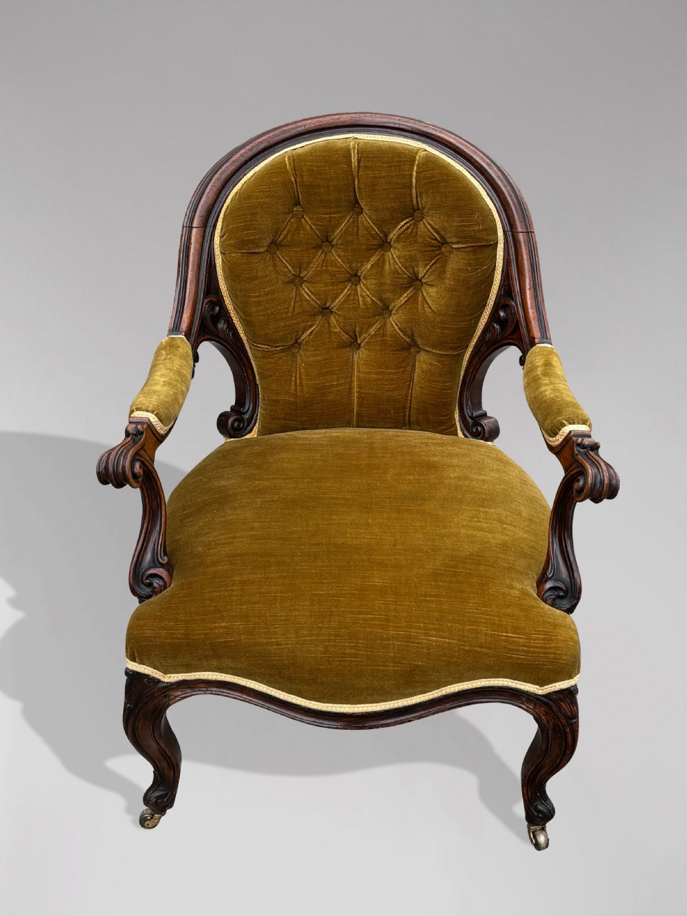 A 19th-century Victorian mahogany armchair upholstered in tufted olive green velvet with carved scroll arms and cabriole legs on brass castors. View III