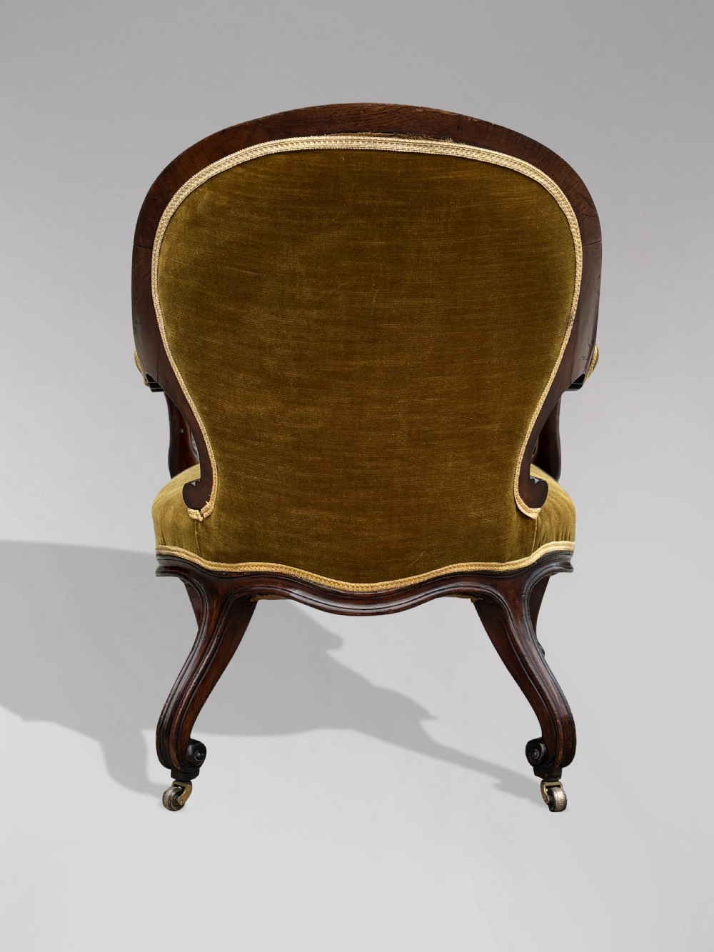 A 19th-century Victorian mahogany armchair upholstered in tufted olive green velvet with carved scroll arms and cabriole legs on brass castors. View IV