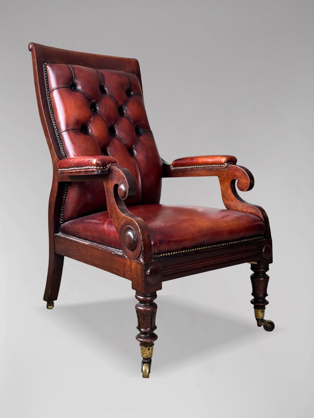 A 19th-century William IV mahogany library armchair featuring deep-buttoned red-brown leather upholstery, scrolled arms, brass stud trim, and turned front legs on brass castors. View II