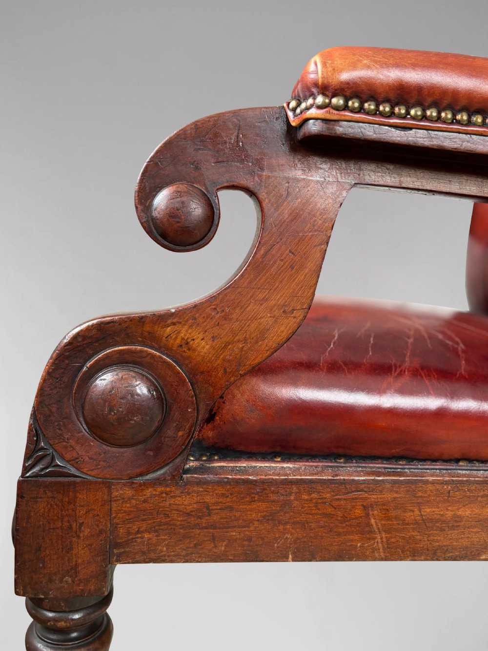 A 19th-century William IV mahogany library armchair featuring deep-buttoned red-brown leather upholstery, scrolled arms, brass stud trim, and turned front legs on brass castors. View VIII