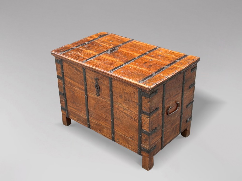 A nineteenth-century Anglo-Indian teak storage trunk featuring heavy iron banding, iron side carrying handles, and an aged timber patina.