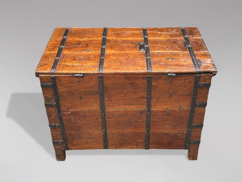 A nineteenth-century Anglo-Indian teak storage trunk featuring heavy iron banding, iron side carrying handles, and an aged timber patina. View V