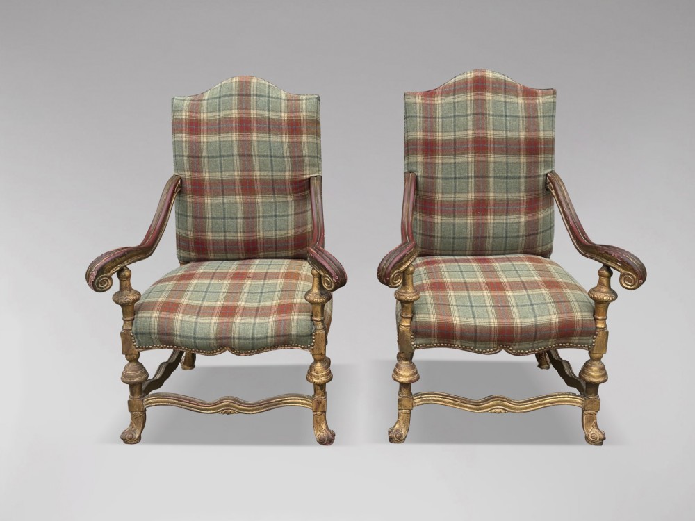 A pair of 19th-century French giltwood throne armchairs upholstered in green and red tartan plaid fabric with carved scroll arms.