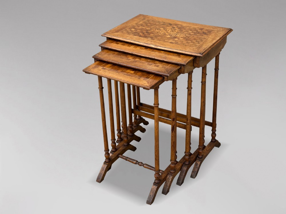 A set of four graduating French walnut nesting tables featuring geometric parquetry tops, central floral marquetry inlays, turned legs, and trestle feet.