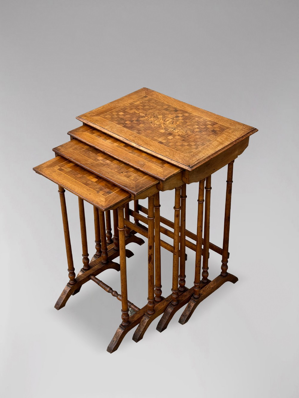 A set of four graduating French walnut nesting tables featuring geometric parquetry tops, central floral marquetry inlays, turned legs, and trestle feet. View II