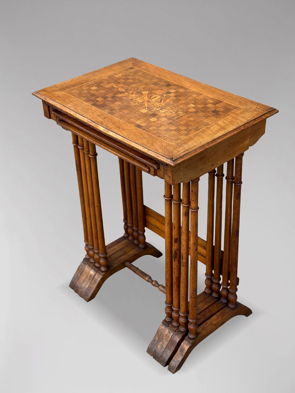 A set of four graduating French walnut nesting tables featuring geometric parquetry tops, central floral marquetry inlays, turned legs, and trestle feet. View III