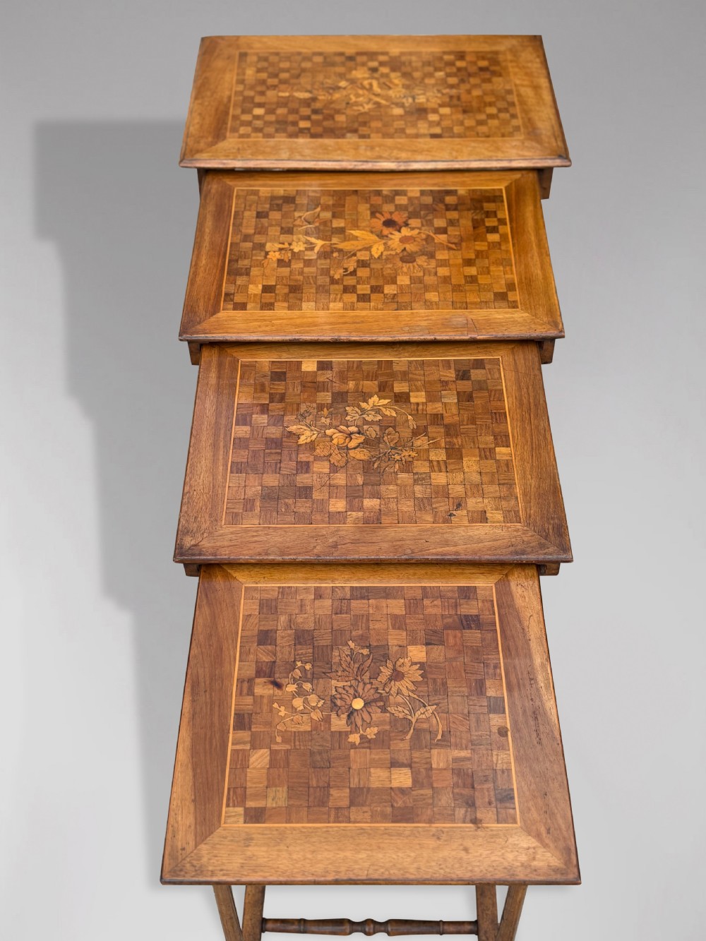 A set of four graduating French walnut nesting tables featuring geometric parquetry tops, central floral marquetry inlays, turned legs, and trestle feet. View IV
