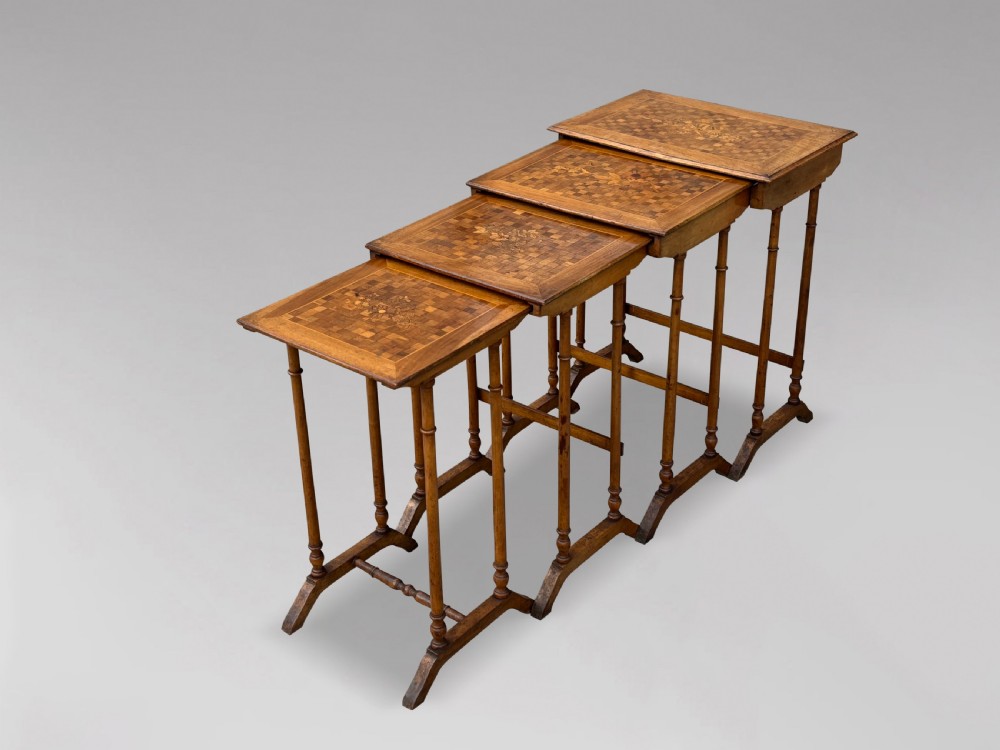 A set of four graduating French walnut nesting tables featuring geometric parquetry tops, central floral marquetry inlays, turned legs, and trestle feet. View V