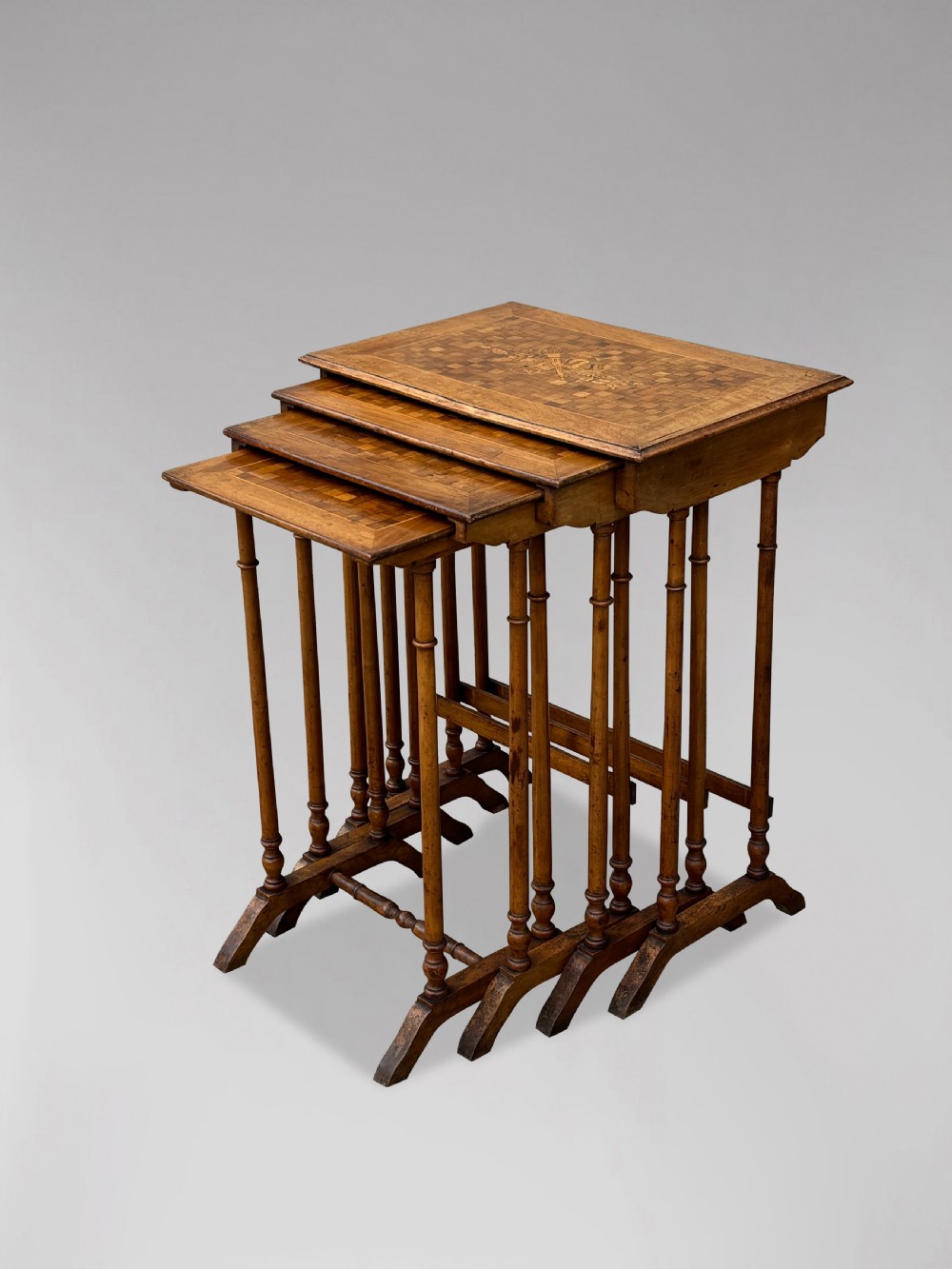 A set of four graduating French walnut nesting tables featuring geometric parquetry tops, central floral marquetry inlays, turned legs, and trestle feet. View VIII