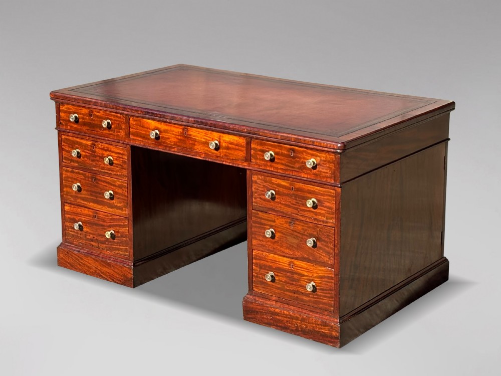 A Victorian flame mahogany partners desk featuring a brown leather inset writing surface, multiple drawers with brass knob handles on twin pedestals, resting on plinth bases.