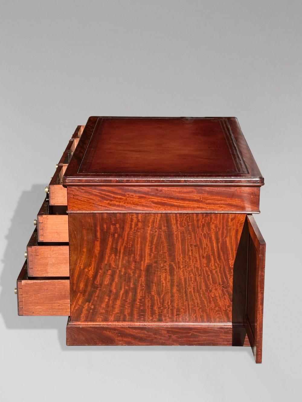A Victorian flame mahogany partners desk featuring a brown leather inset writing surface, multiple drawers with brass knob handles on twin pedestals, resting on plinth bases. View III