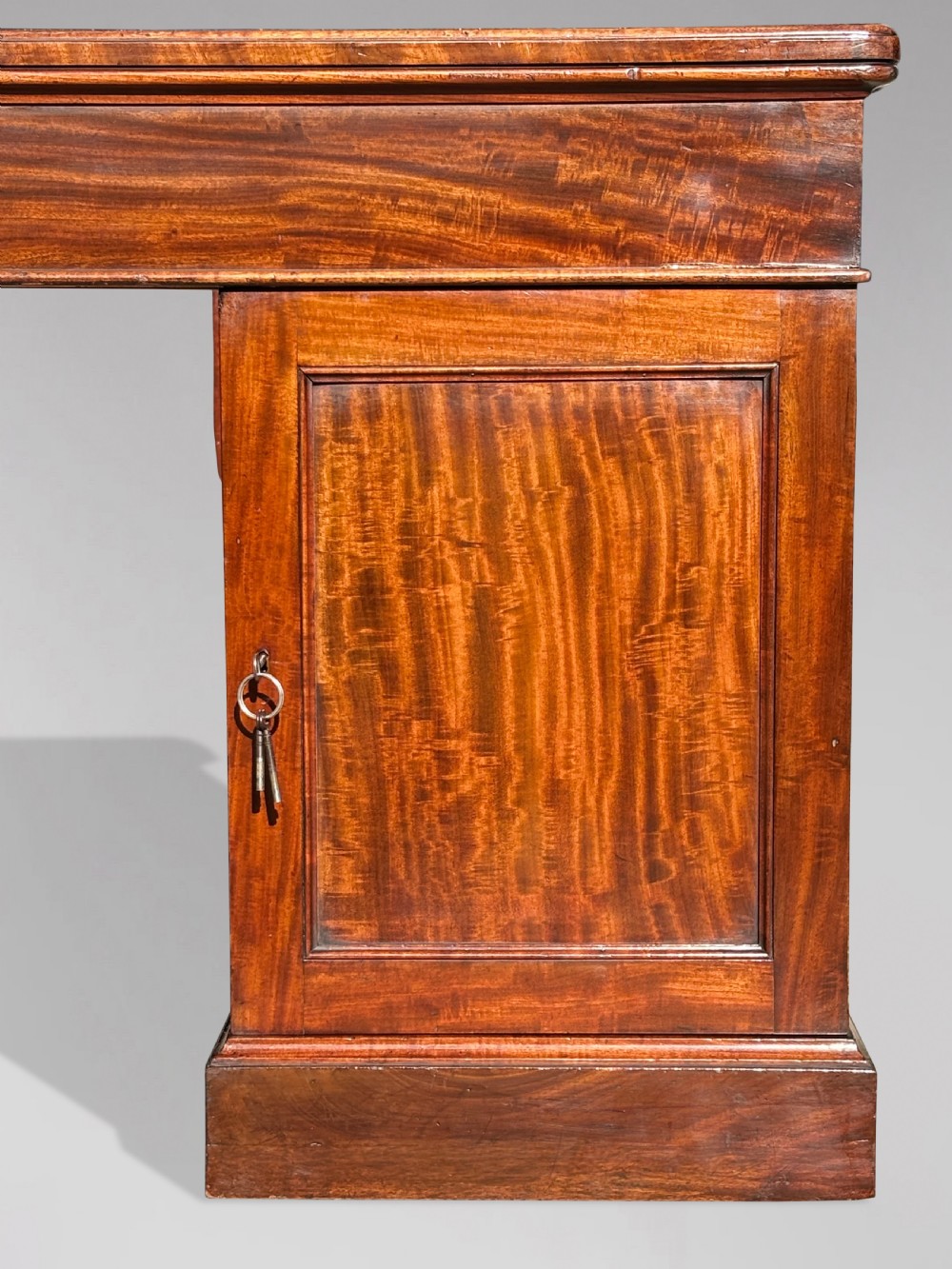 A Victorian flame mahogany partners desk featuring a brown leather inset writing surface, multiple drawers with brass knob handles on twin pedestals, resting on plinth bases. View IV