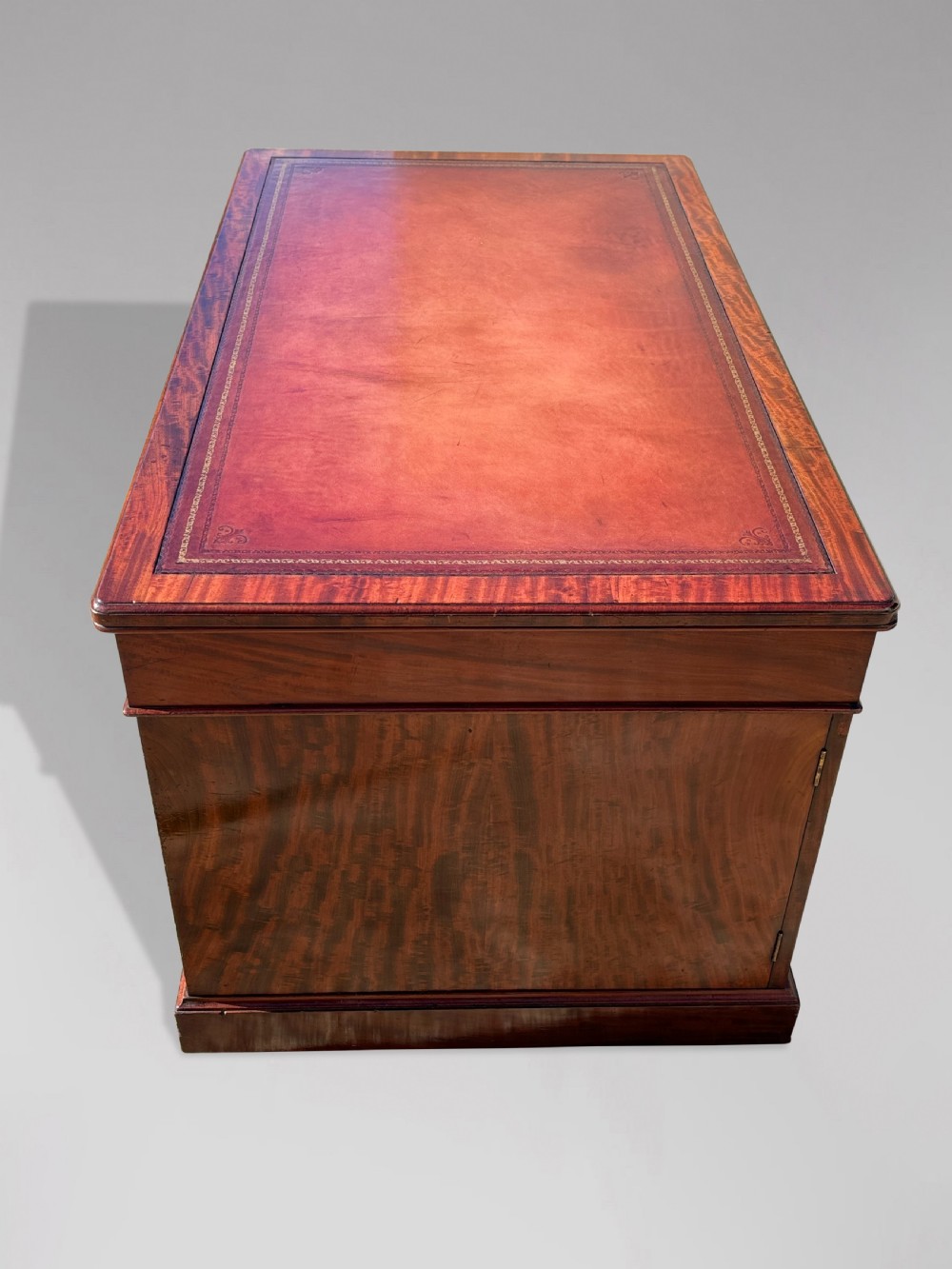 A Victorian flame mahogany partners desk featuring a brown leather inset writing surface, multiple drawers with brass knob handles on twin pedestals, resting on plinth bases. View V